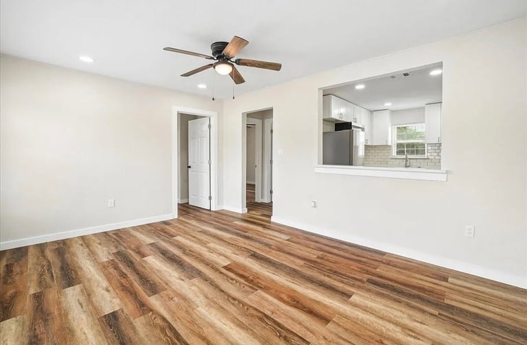 Empty bedroom with wood-grain vinyl flooring, white walls, ceiling fan, and two white doors opening to other rooms