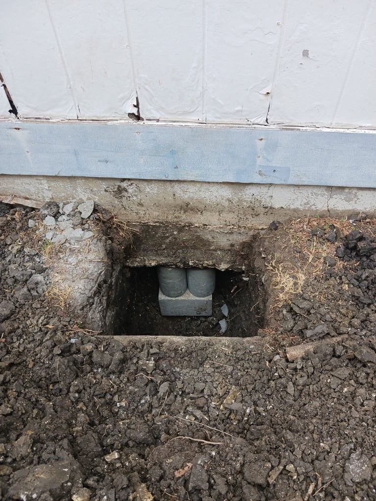 Underground duct with gray metal pipes visible through opening in deteriorating concrete foundation