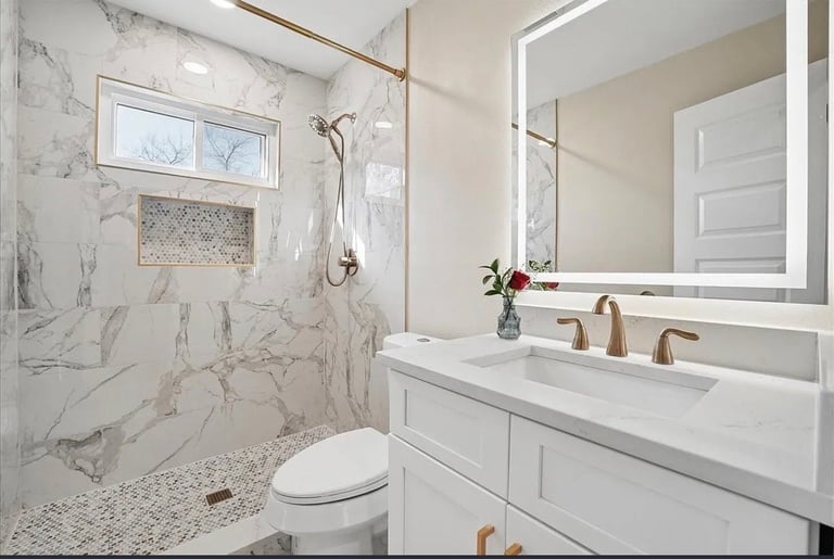 Modern luxury bathroom with marble tile shower, white vanity, illuminated mirror, and marble-tiled shower floor with glass enclosure