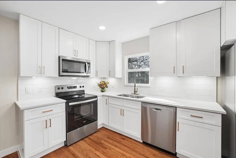 Modern white kitchen with stainless steel appliances, white cabinets, subway tile backsplash, and hardwood flooring