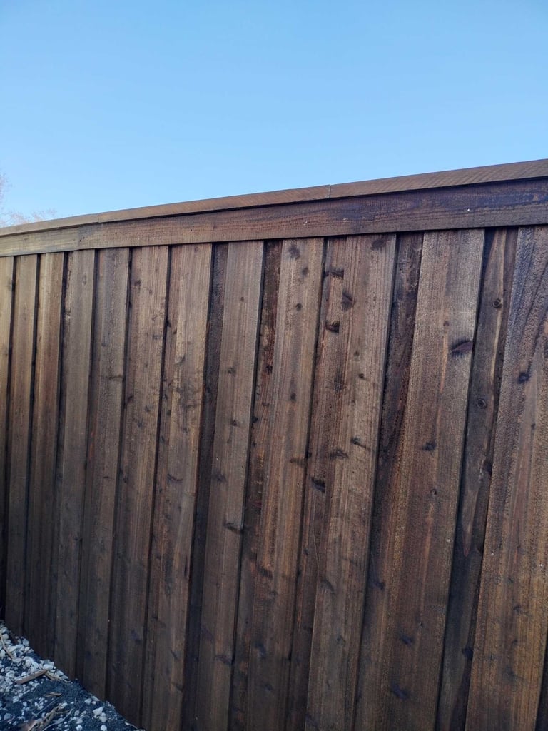 Dark wooden fence with vertical planks and metal brackets against a clear blue sky