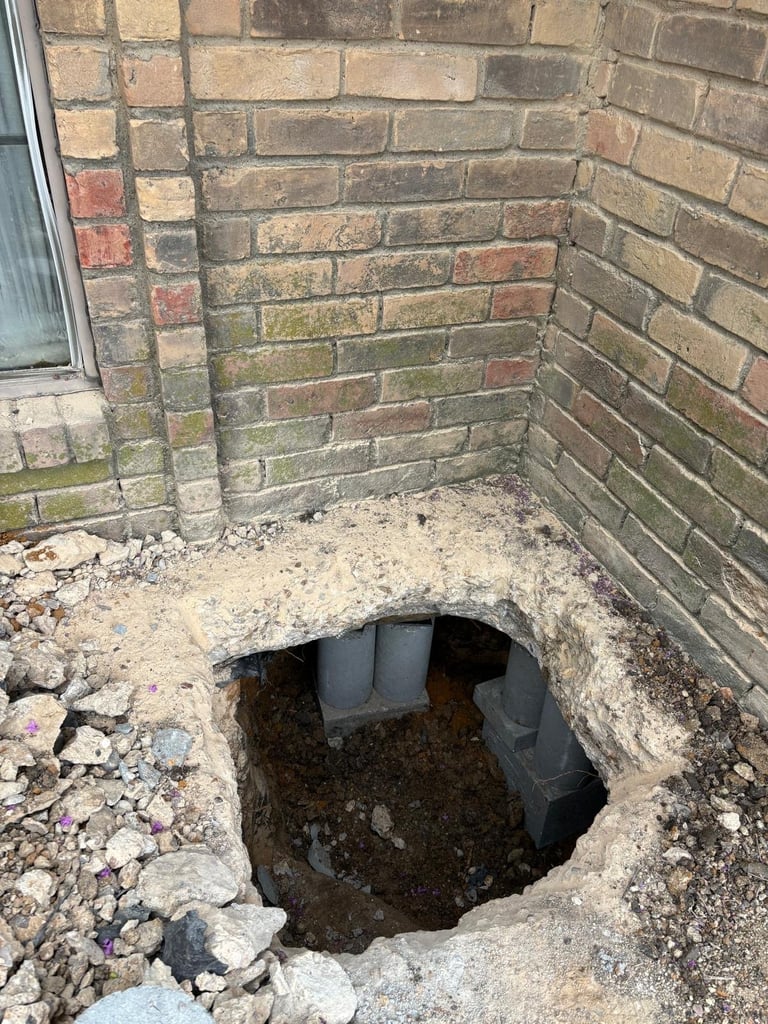 Underground cavity beneath brick patio with plastic pipes visible in dark soil
