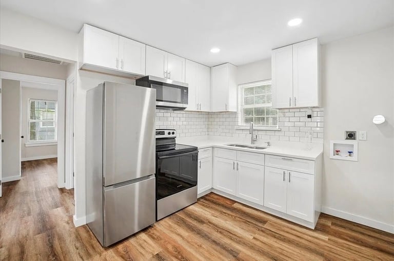 Modern kitchen with white cabinetry, stainless steel appliances, subway tile backsplash, and wood-look flooring